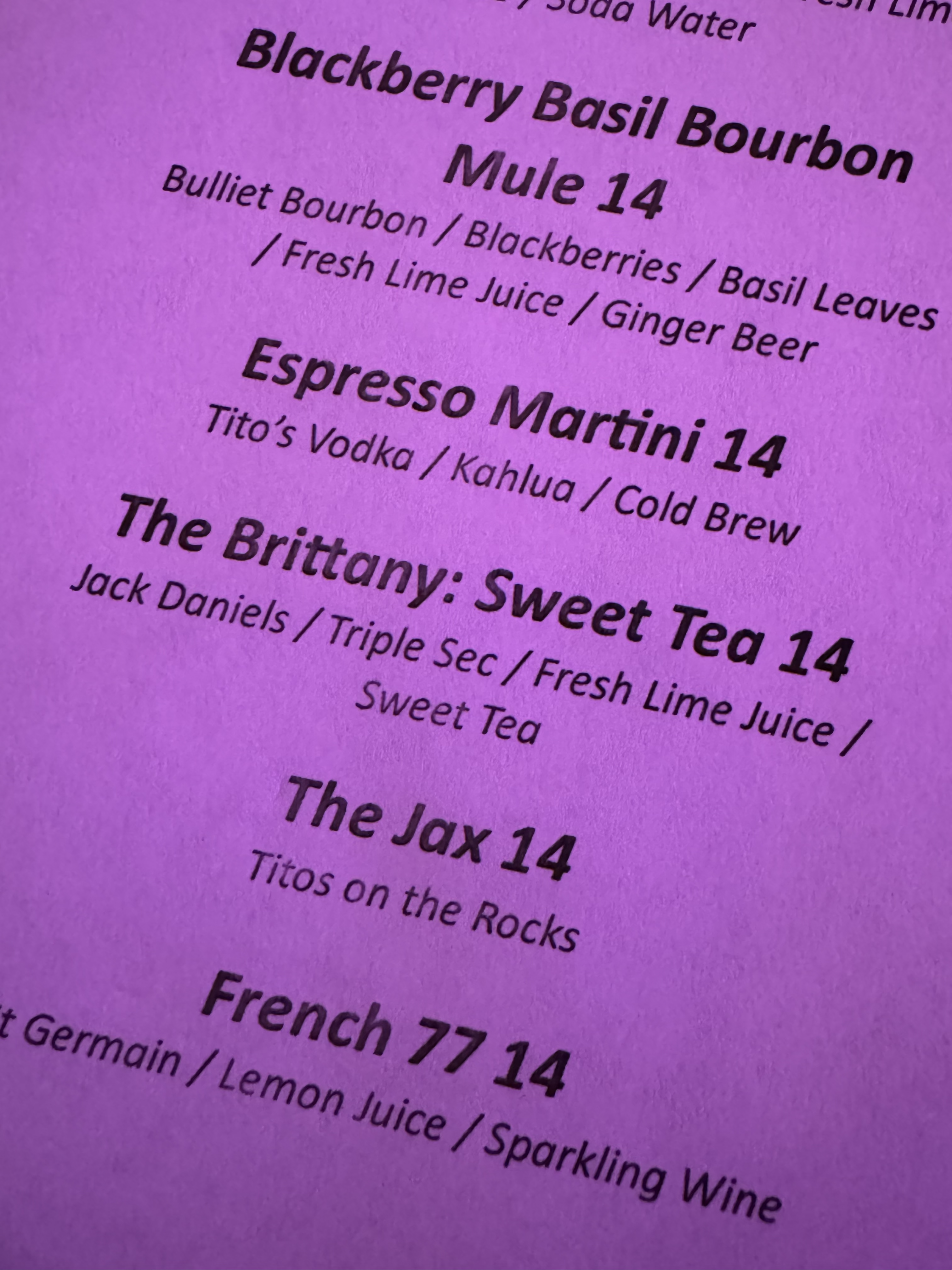A close-up of a menu displaying a selection of drinks including Bourbon Basil Bourbon, Espresso Martini, The Britney, and French 77