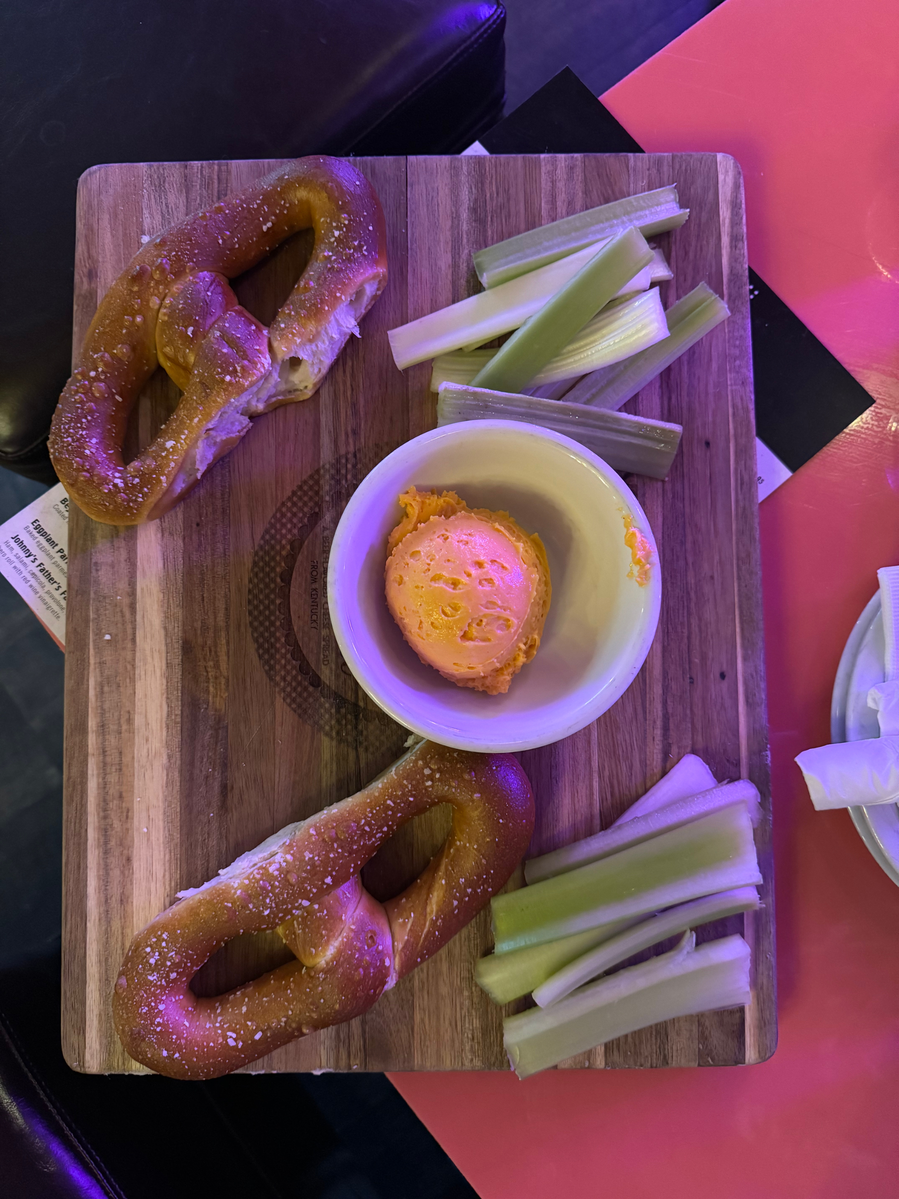 Pretzels, celery, and a bowl of cheese dip on a wooden serving board