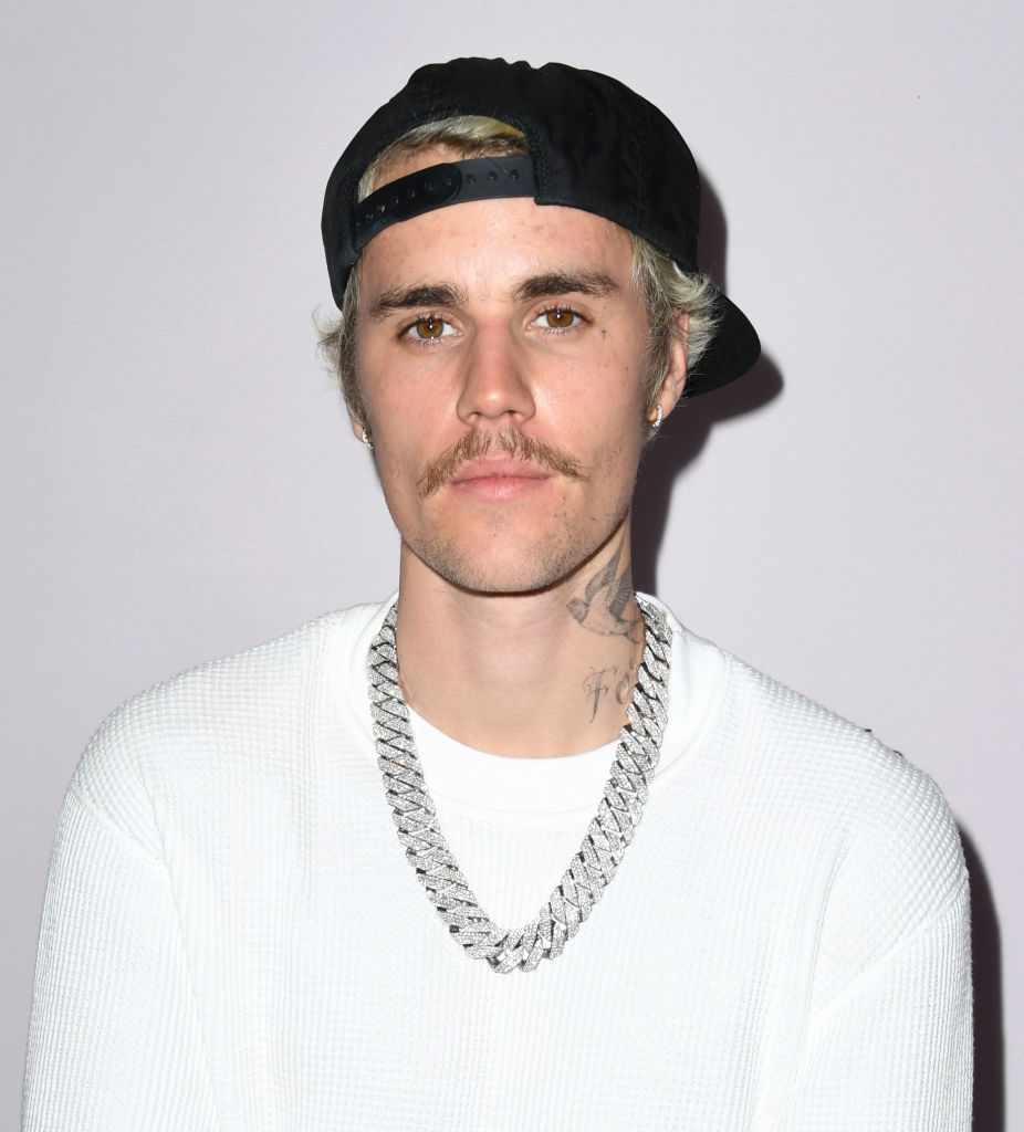 Justin Bieber wearing a white shirt and a black hat, with a thick silver chain necklace