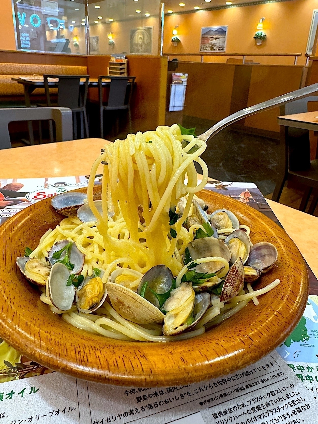 フォークで持ち上げられたボンゴレのパスタが皿に盛られているレストランのテーブルの上にあります。