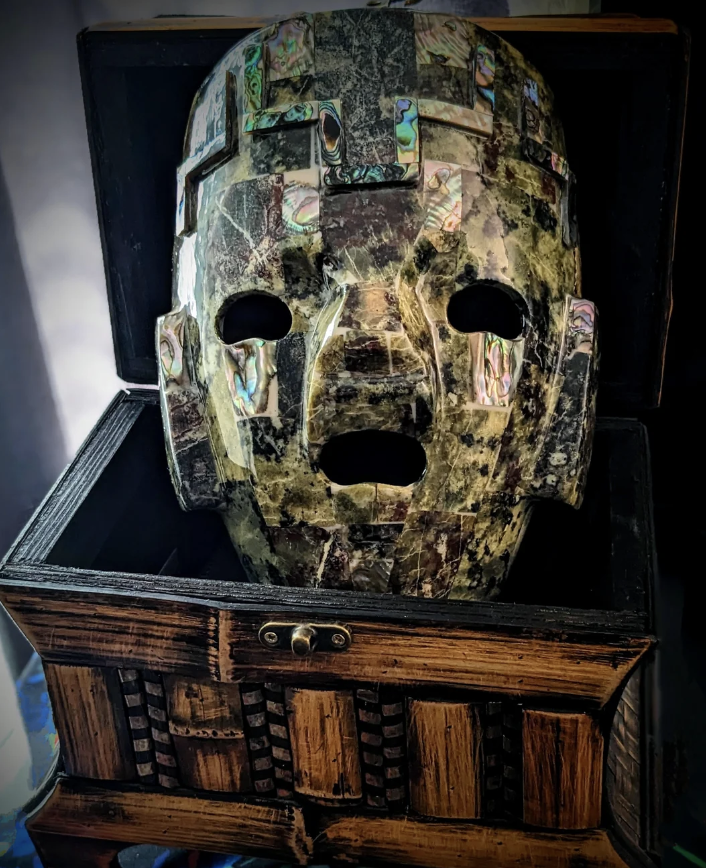 Ornate mask with abstract design displayed in a wooden chest, evoking curiosity and mystery