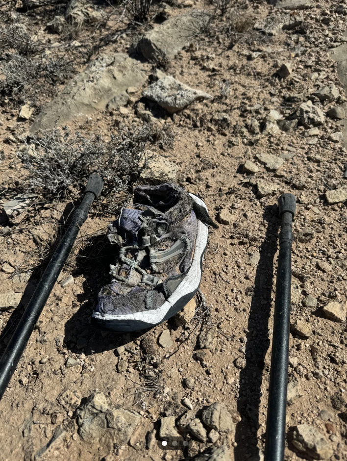 Worn-out shoe on rocky ground between two trekking poles, suggesting a hiker&#x27;s challenging journey