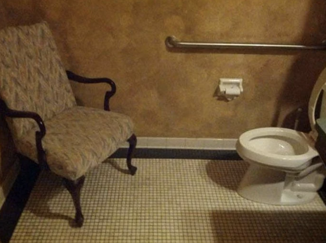 An upholstered chair placed awkwardly close to a toilet in a small bathroom