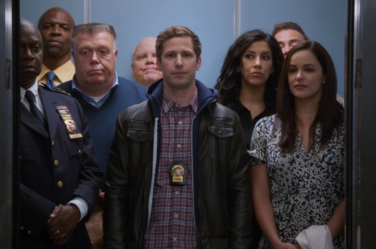 Cast of Brooklyn Nine-Nine standing in an elevator, looking forward