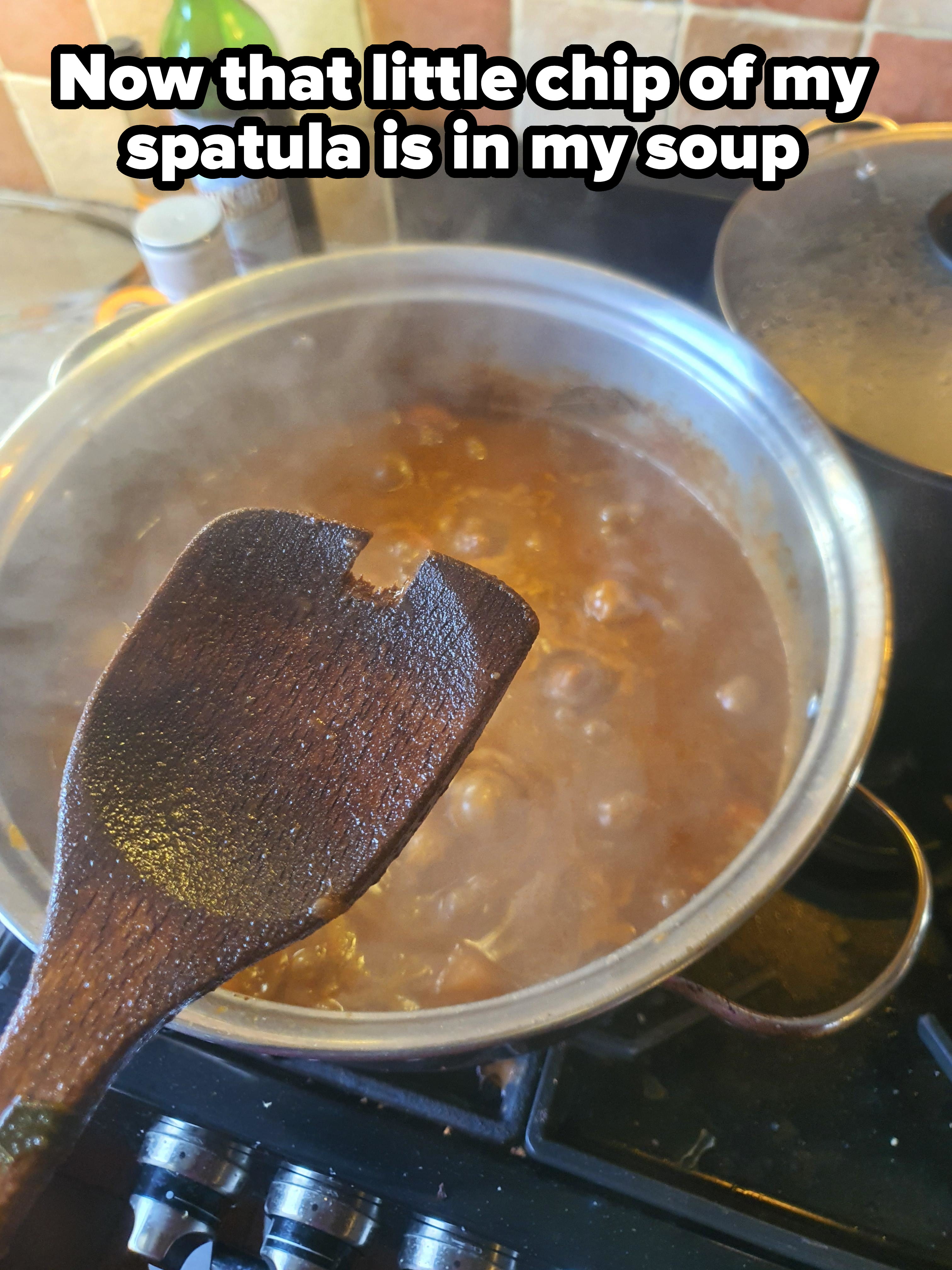 A wooden spoon held over a pot of boiling soup on a stove