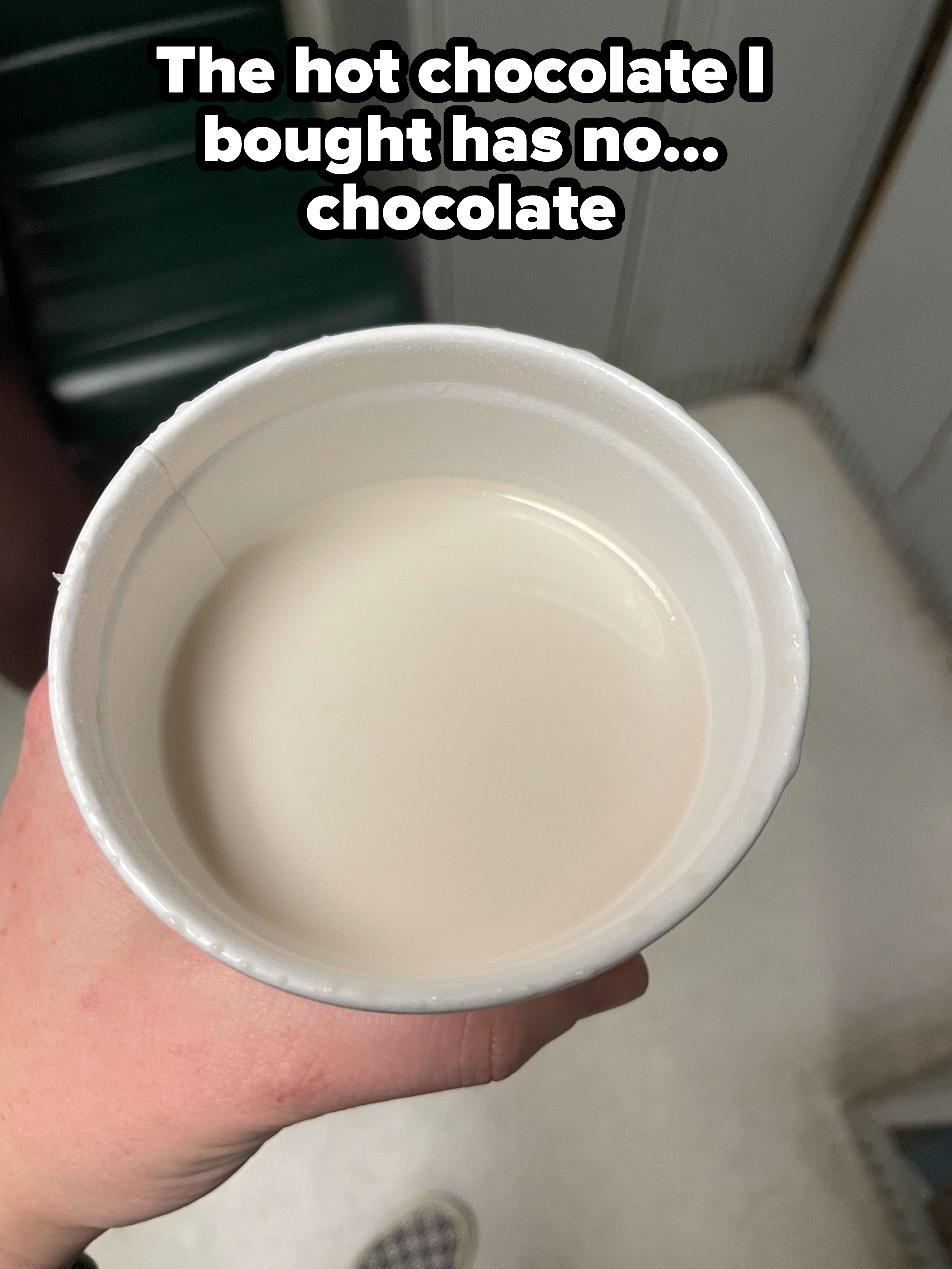 Person holding a styrofoam cup filled with a white liquid, possibly milk, indoors