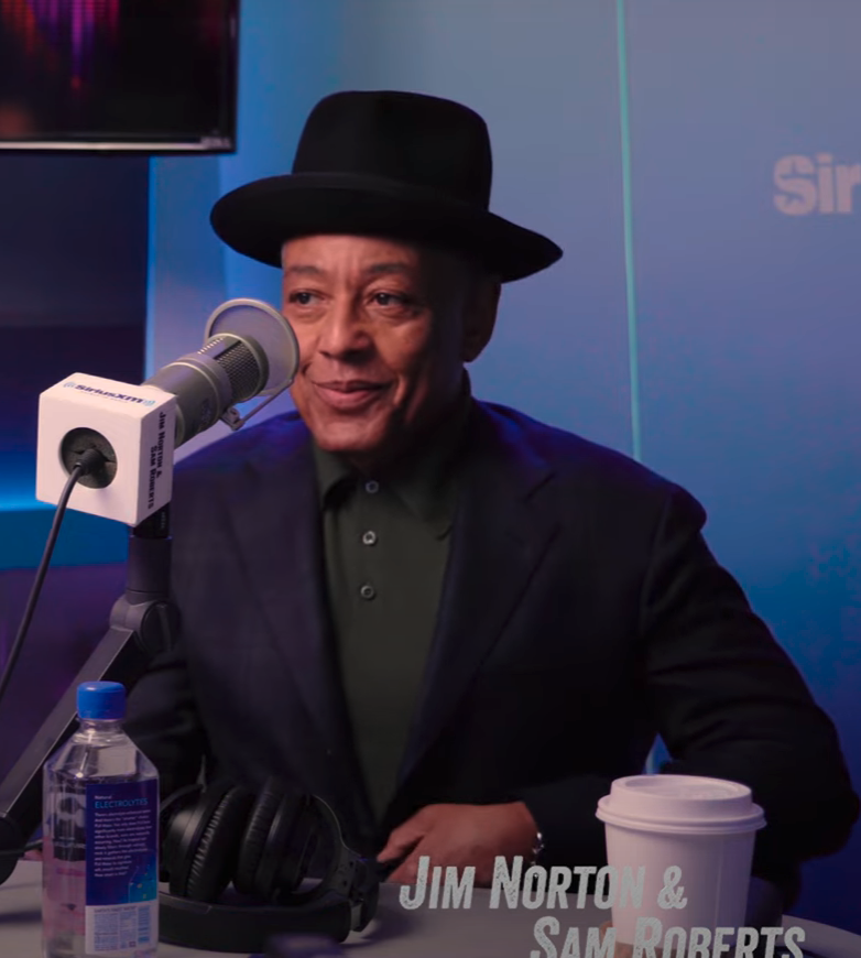 Giancarlo Esposito in a studio wearing a hat and sitting in front of a microphone