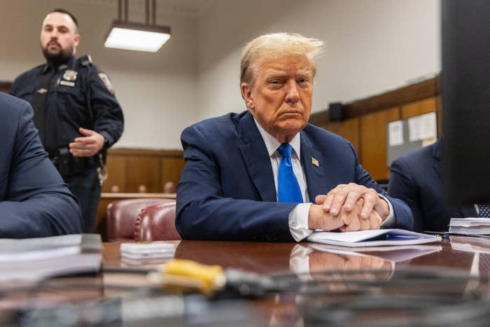 Former President Donald Trump seated at a desk with clasped hands in court