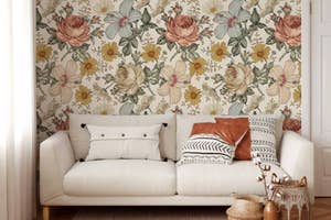 A sofa with mixed pattern pillows against a floral wallpaper, suggesting a cozy home decor style for shopping content