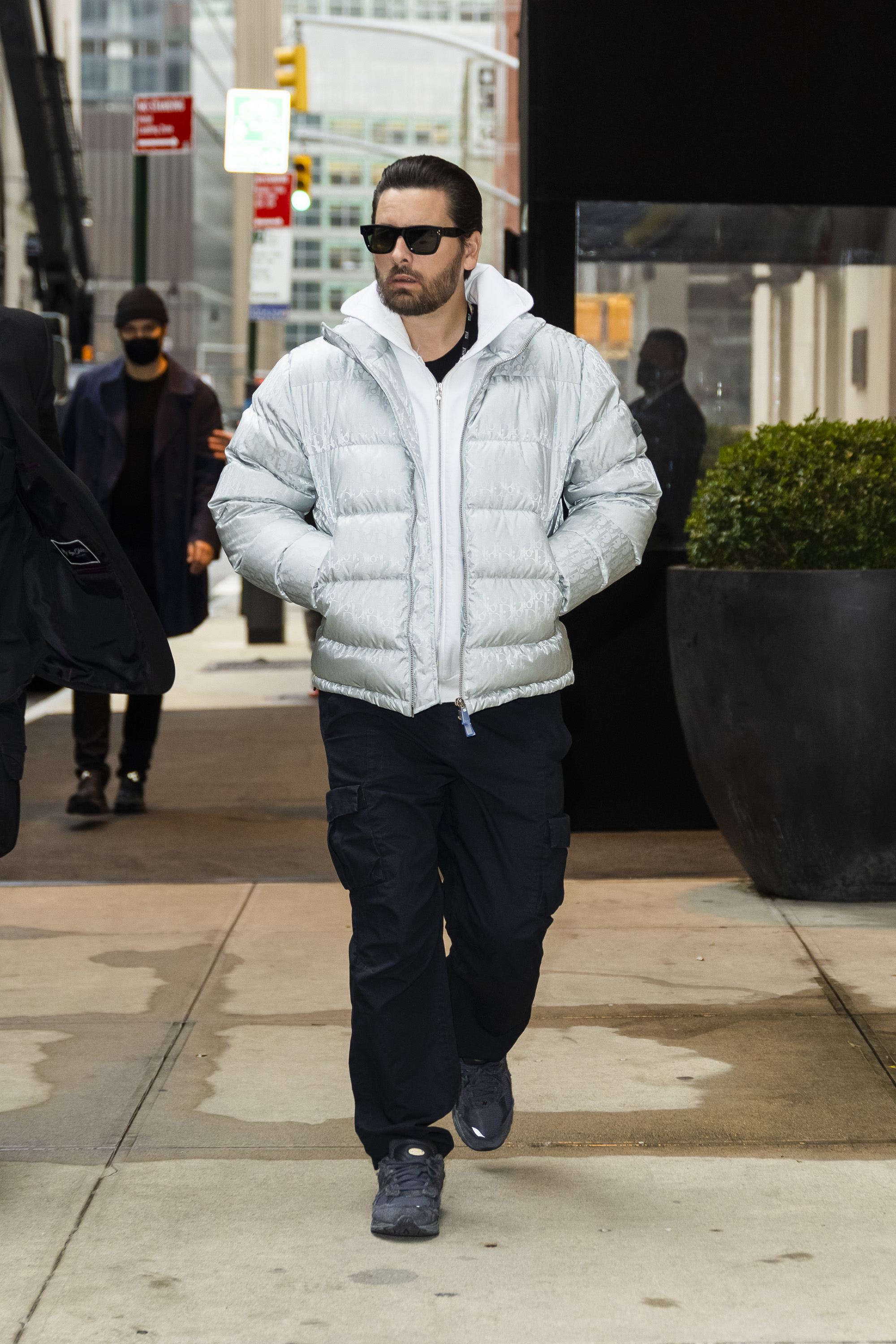 Scott walking down the street while wearing a puffy jacket and sunglasses