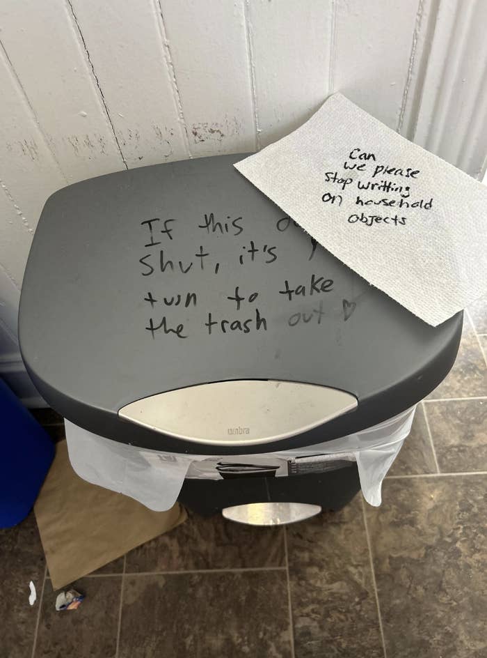 Handwritten note on a trash bin lid saying to shut it properly or take out the trash, with a &quot;Can Please Stop Putting Sharpie on Household Objects&quot; note