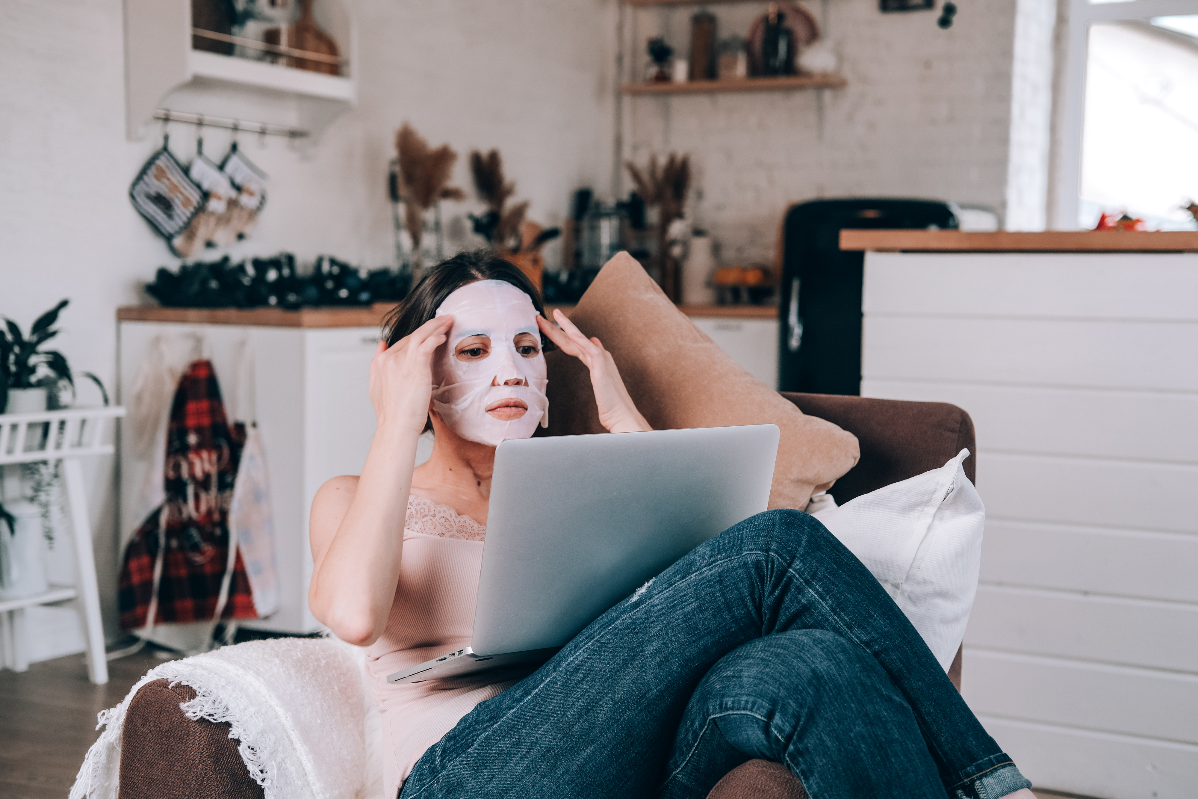 Woman wearing a sheet mask while using a laptop at home