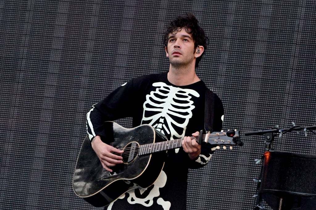 Matty in a skeleton-themed outfit playing guitar onstage