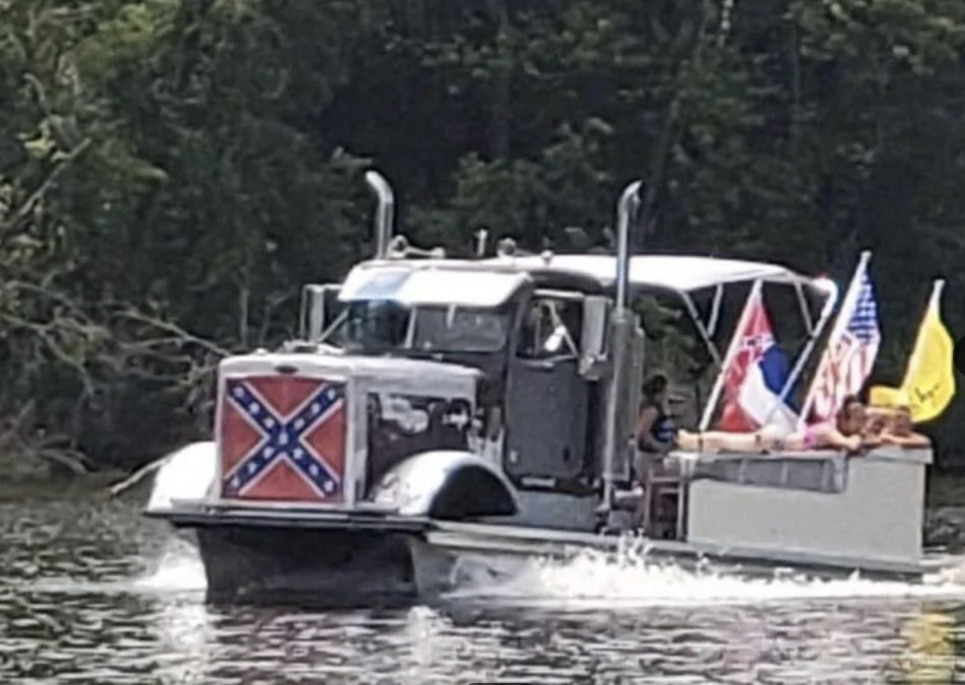 Semi-truck cab converted into a boat with flags, carrying people on a river