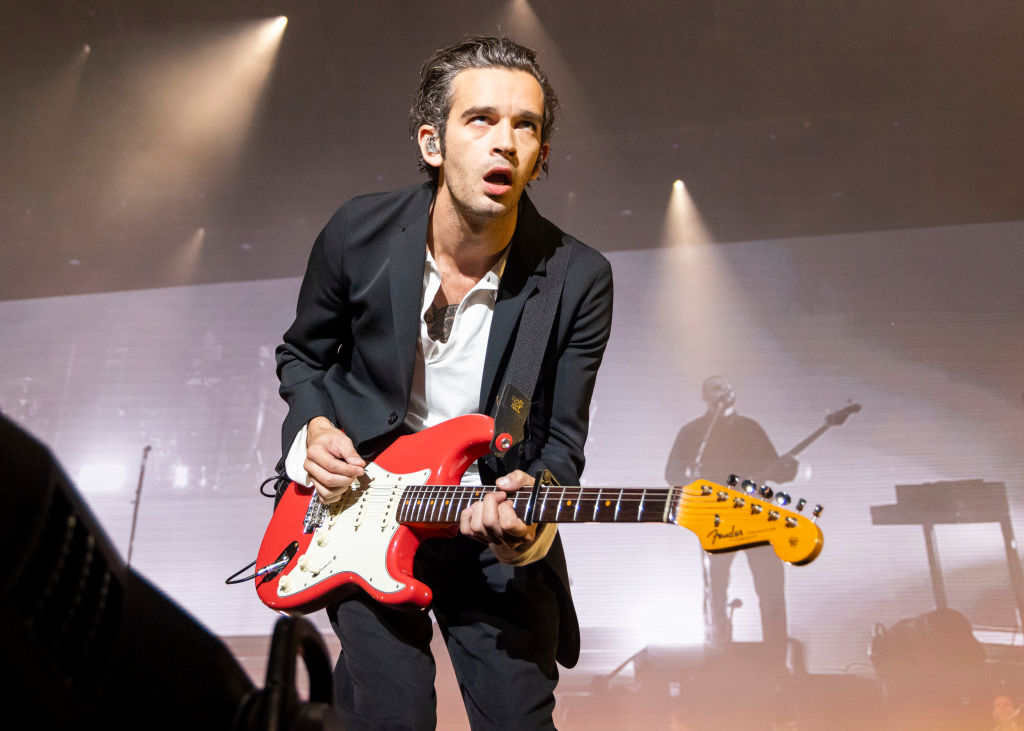 Matty in a suit playing an electric guitar on stage during a concert