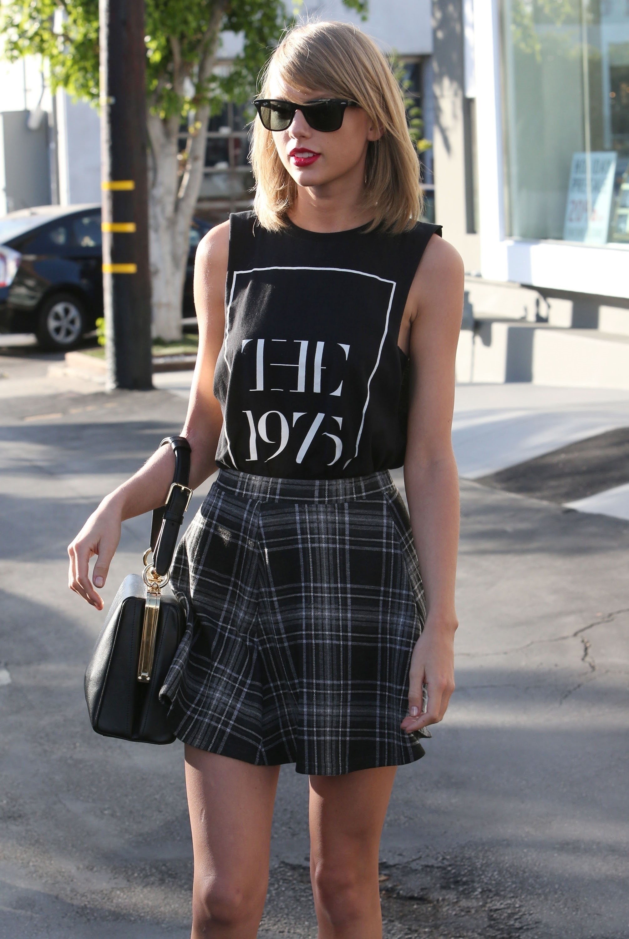 Taylor Swift in a sleeveless &quot;The 1975&quot;  top and plaid skirt, wearing sunglasses and carrying a handbag