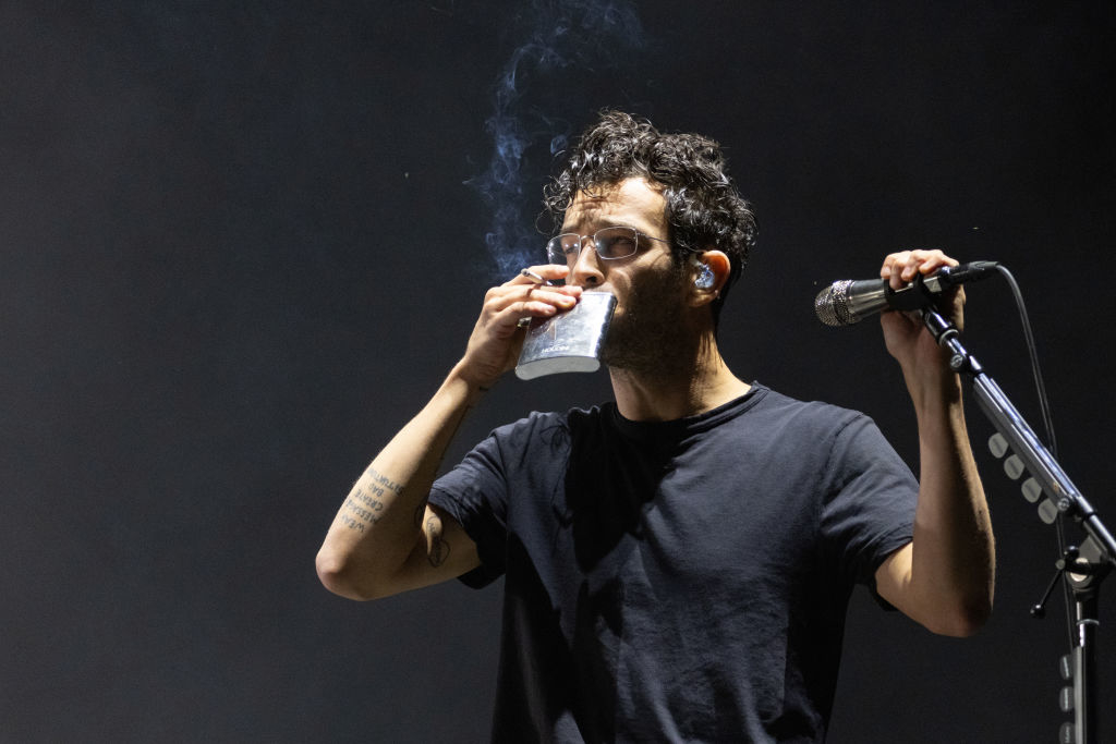 Matty onstage with taking a swig from a flask while holding a lit cigarette