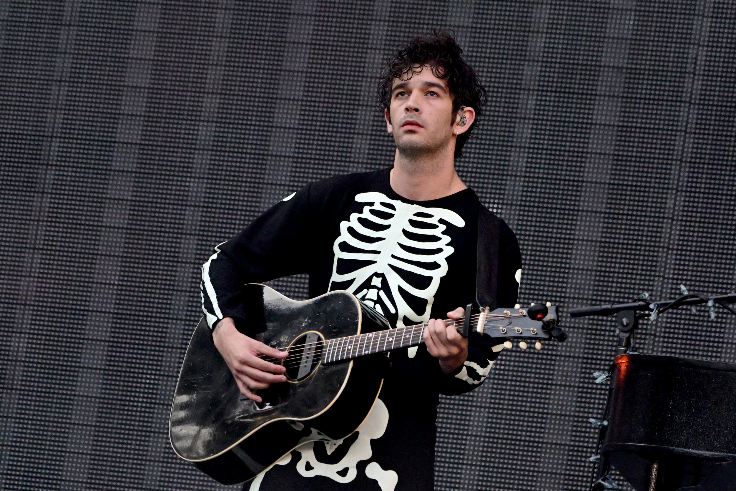 Matty Healy en escenario con guitarra y camiseta con estampado de esqueleto