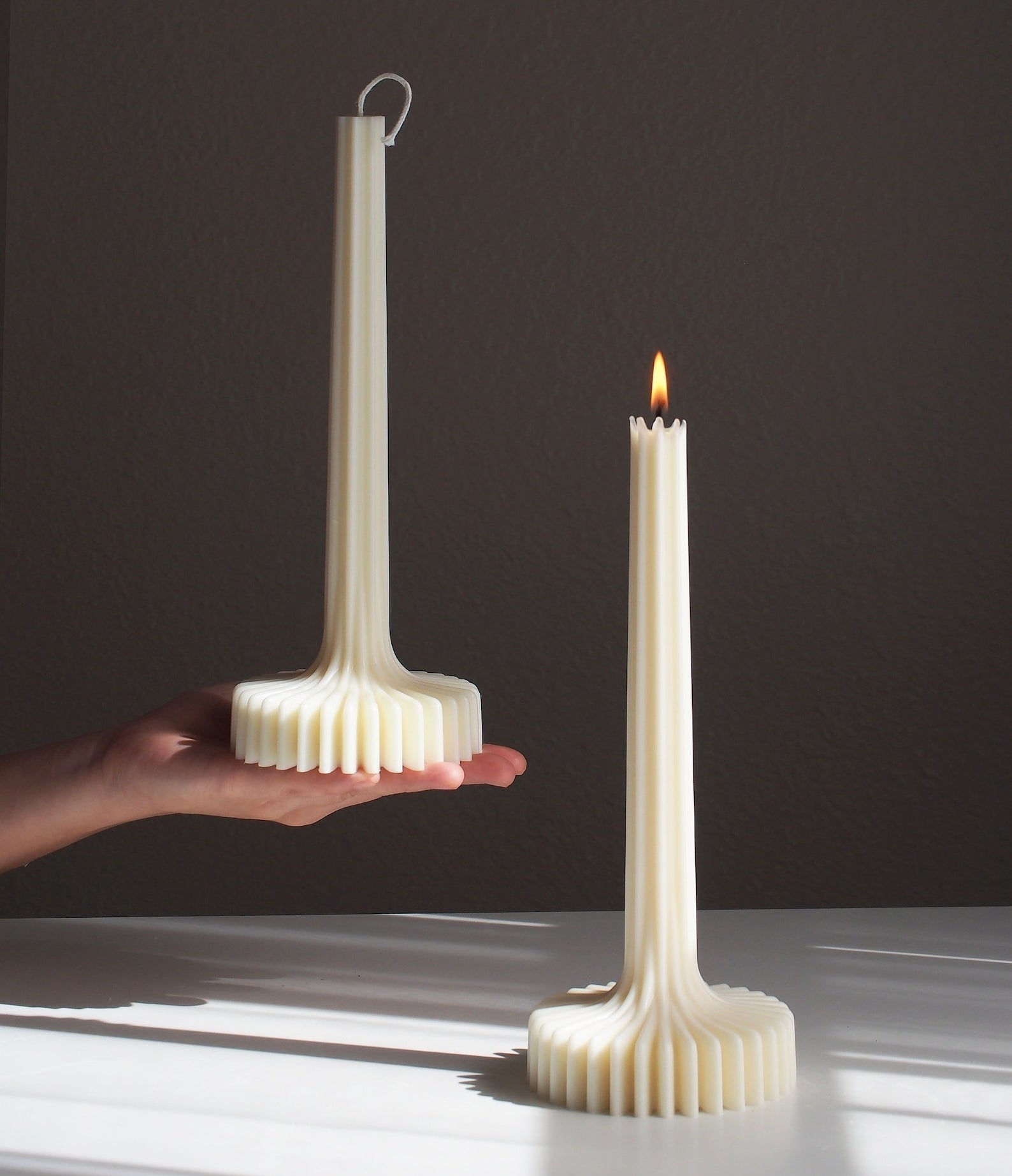 Person holding an unlit ribbed candle similar to the lit one standing on a surface