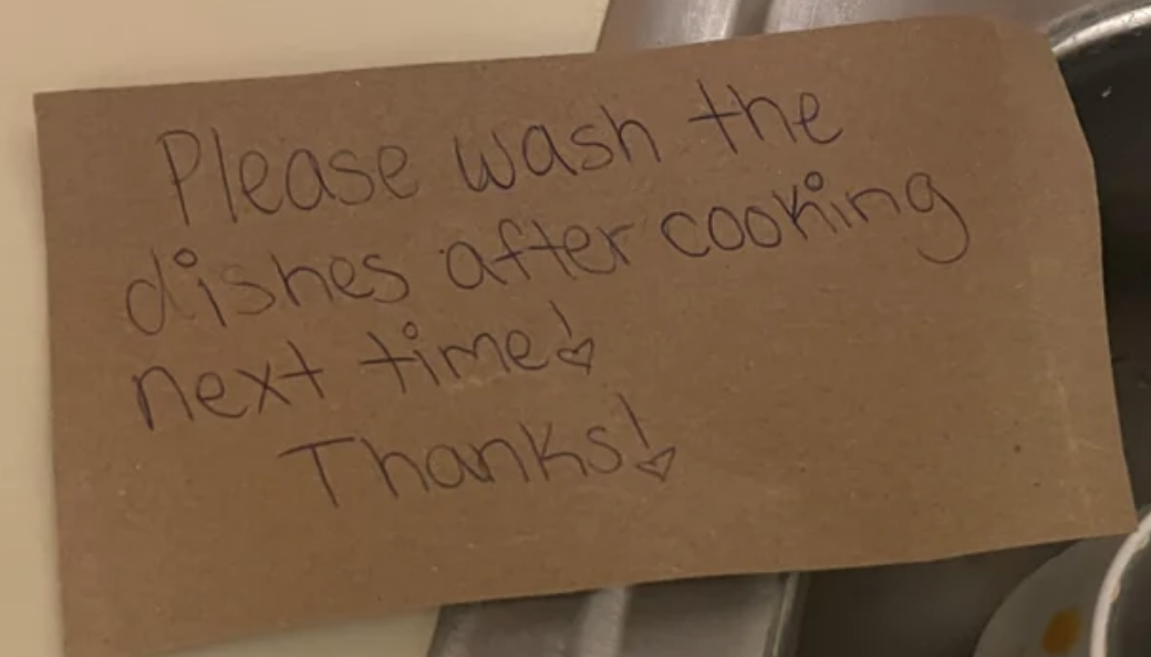 Handwritten note in a sink requesting dishes to be washed after cooking