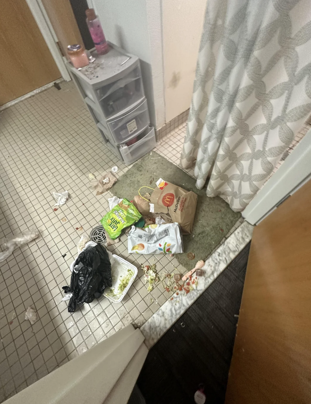 A cluttered bathroom floor with various personal items and trash strewn around