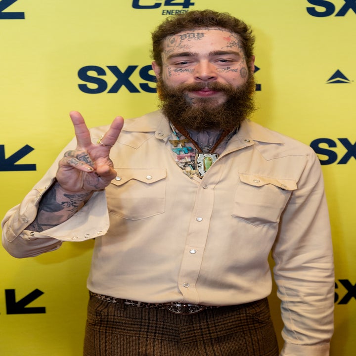 Post Malone in a button-up shirt and plaid pants, making peace sign while at an event
