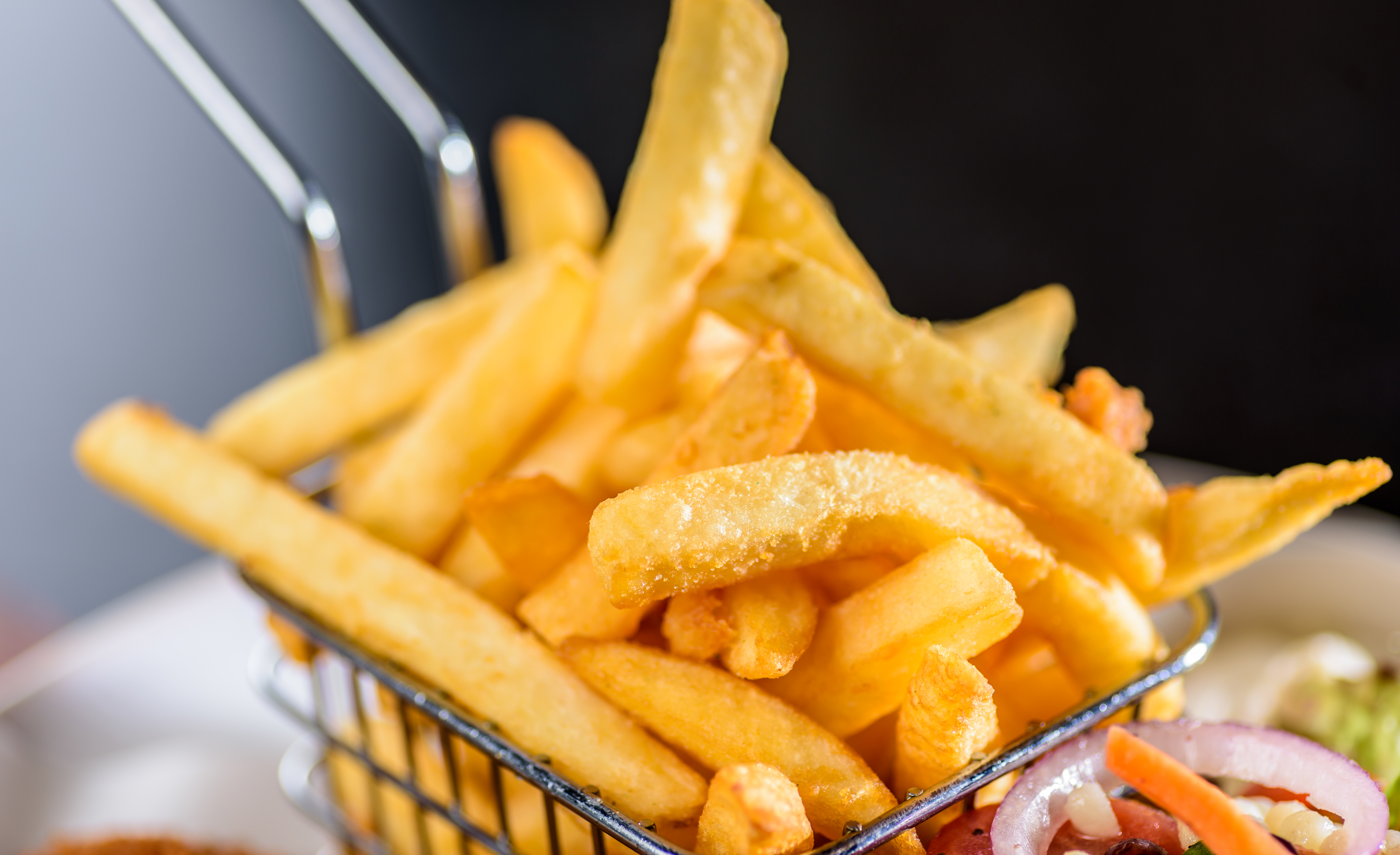 A basket of crispy french fries served beside a salad