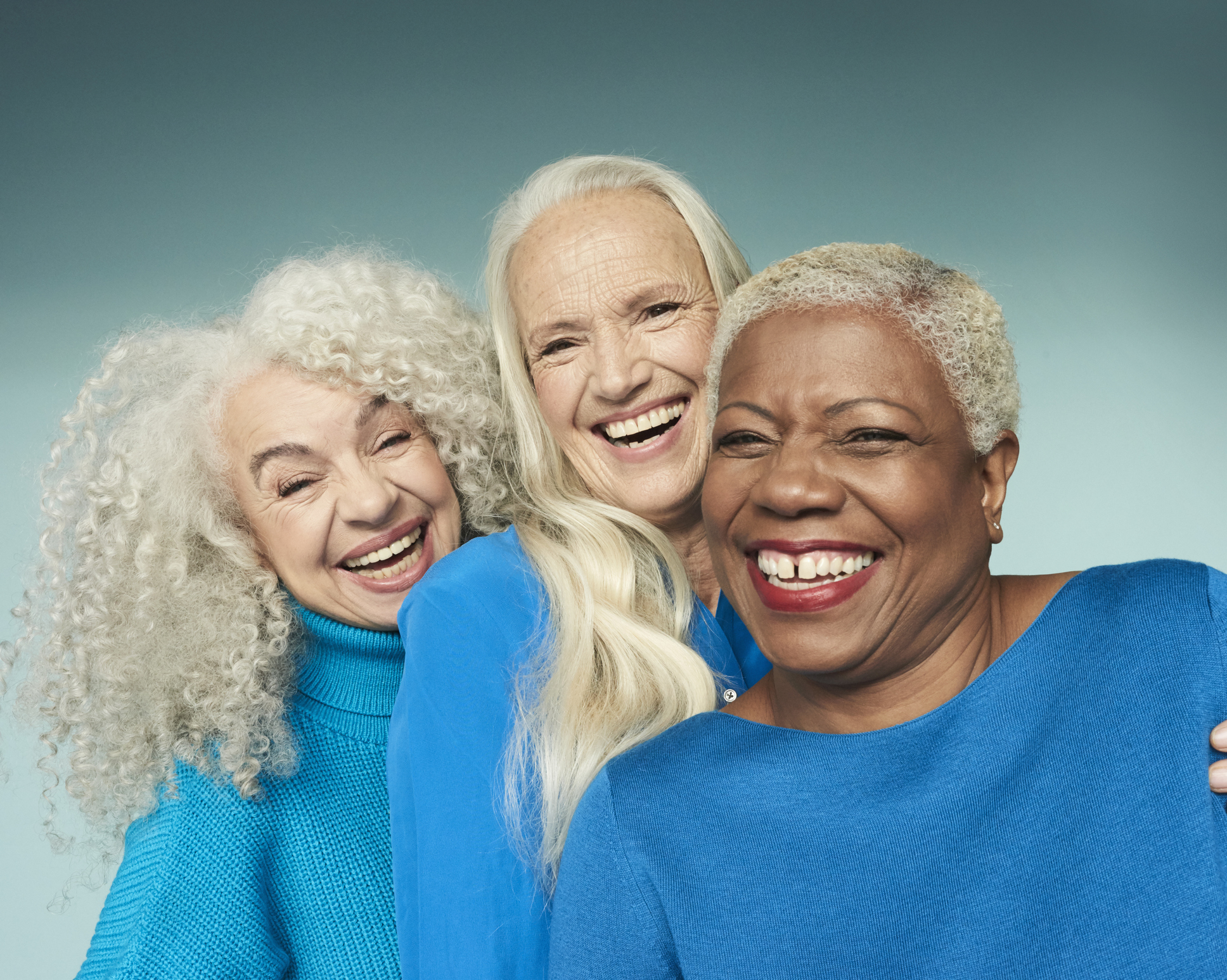 Three joyful women embracing, wearing casual sweaters