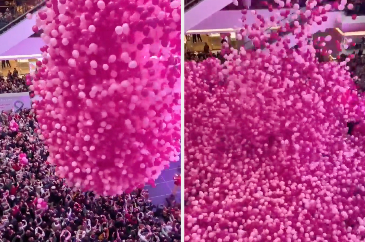 A crowd of people watching a massive pink balloon release indoors