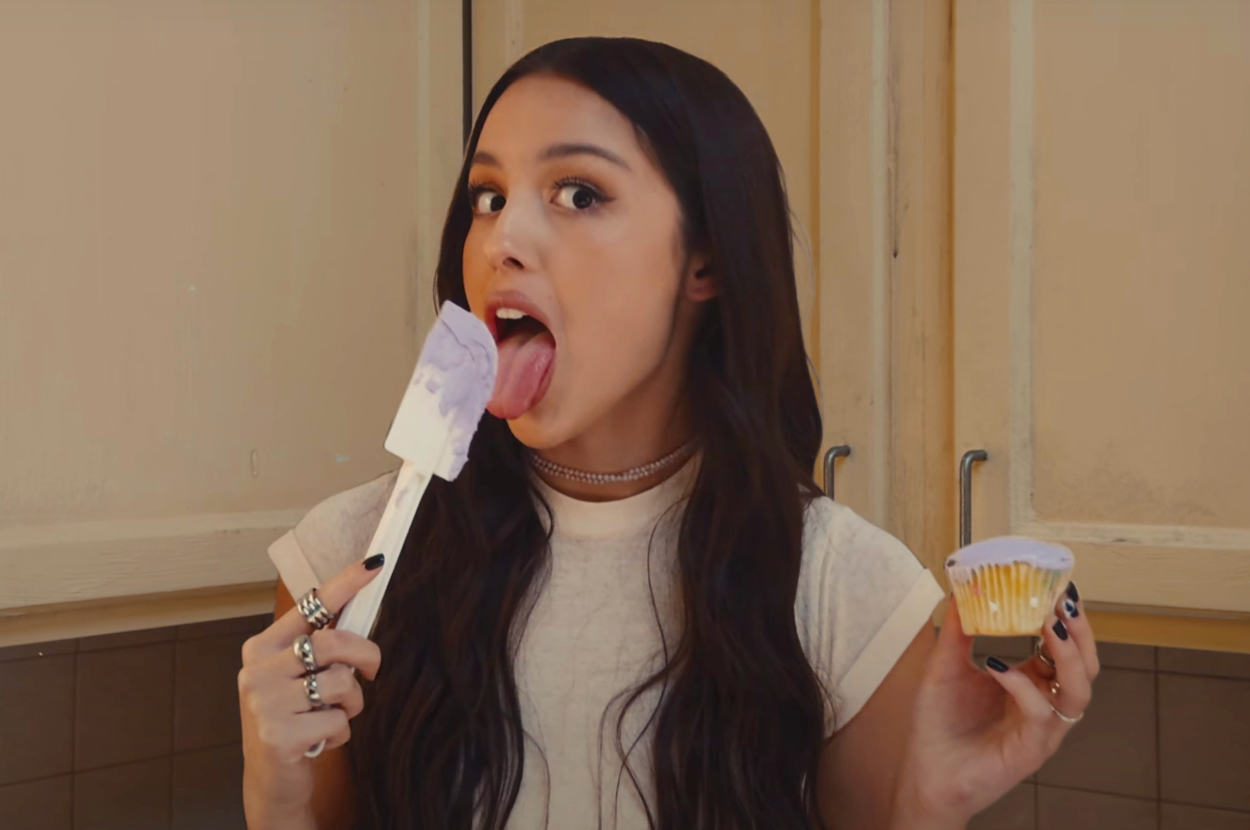 Olivia Rodrigo licking a spatula and holding a cupcake in the Get Him Back music video