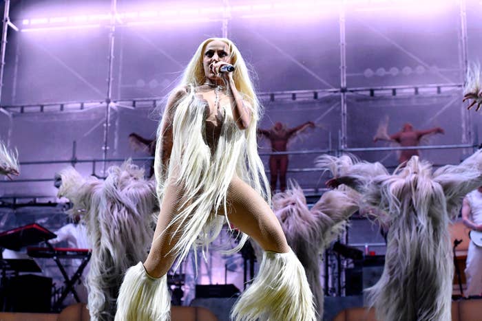 Performer in a fringe outfit singing on stage with dancers in background