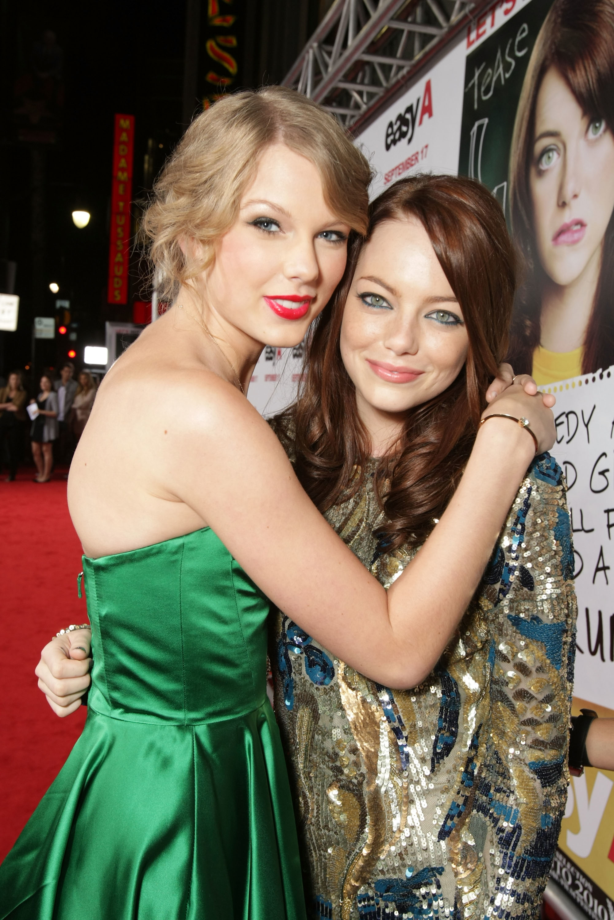 Taylor Swift wearing a green dress, Emma Stone in a sequined outfit, smiling together on the red carpet