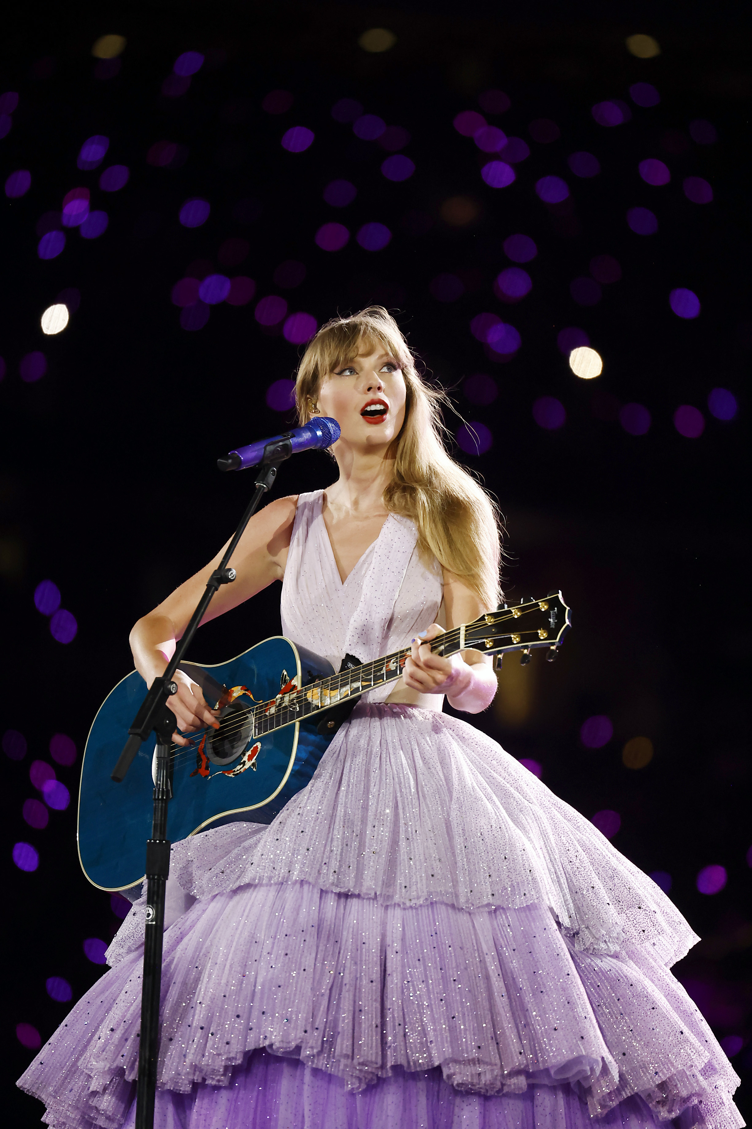 Taylor Swift performing on stage with a guitar, wearing a sparkling ball gown