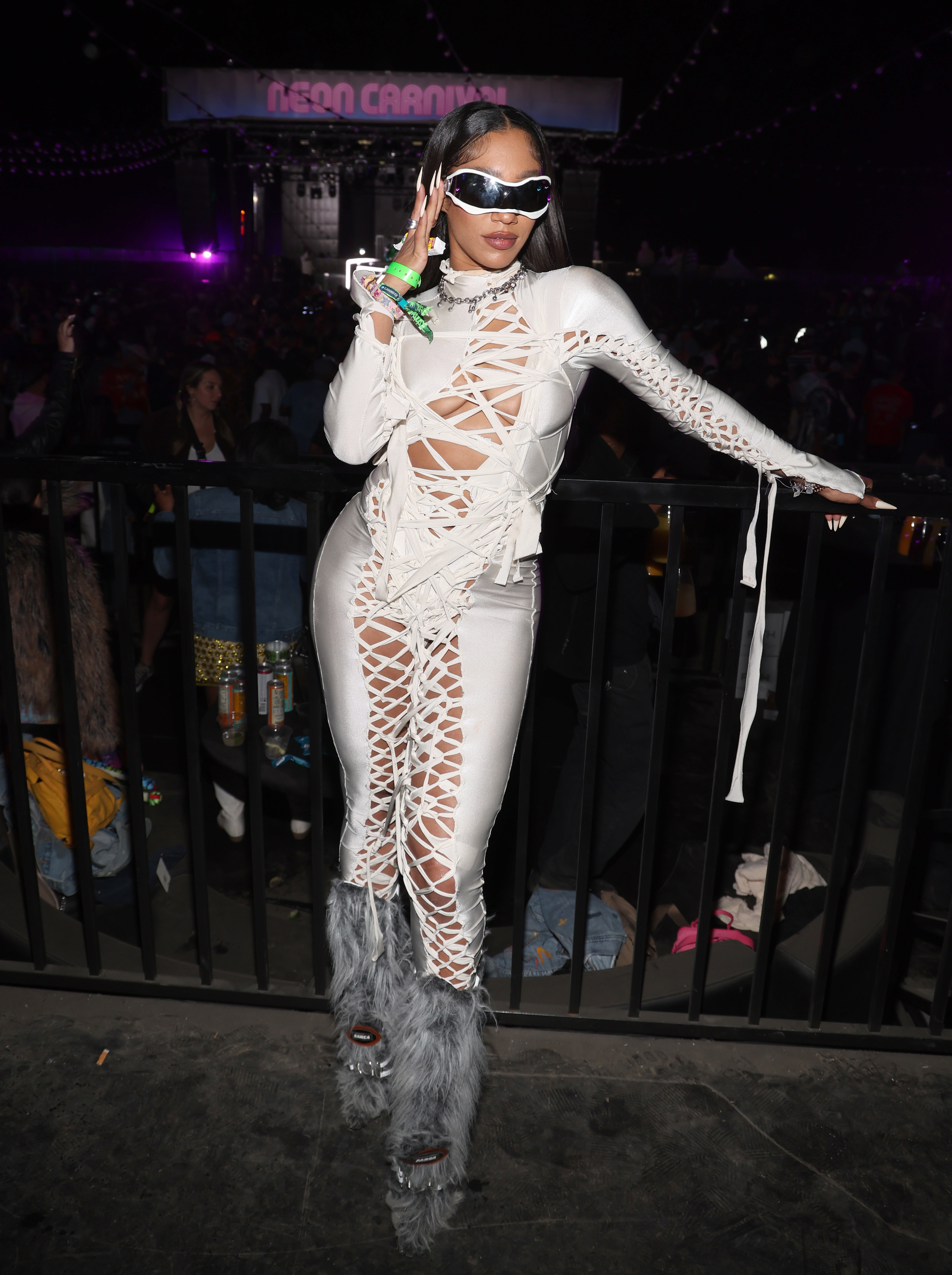 Celebrity in a white cut-out jumpsuit with feather details, standing at an event, wearing sunglasses and holding a drink