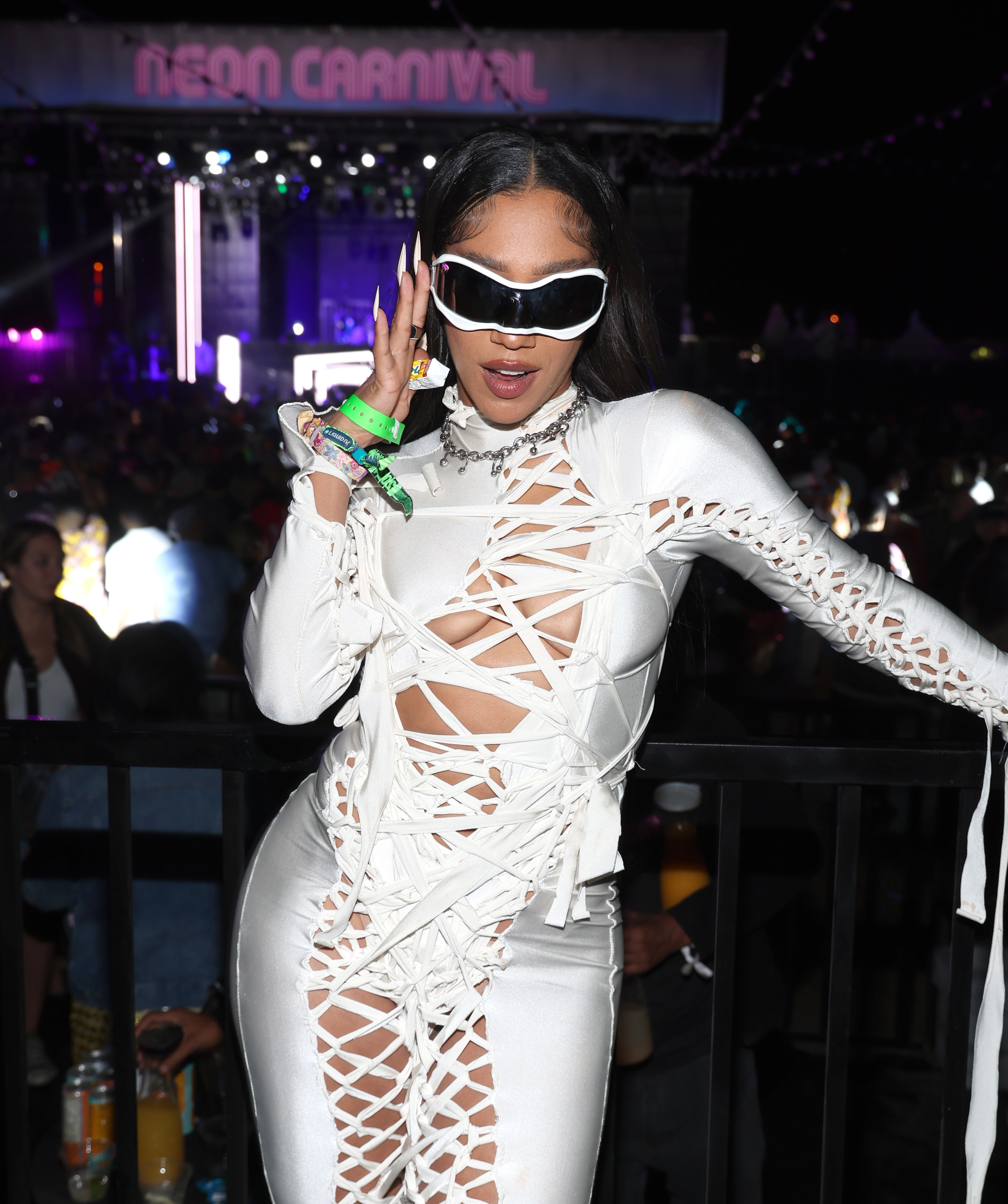 Person in a white cut-out outfit and sunglasses posing with a peace sign gesture