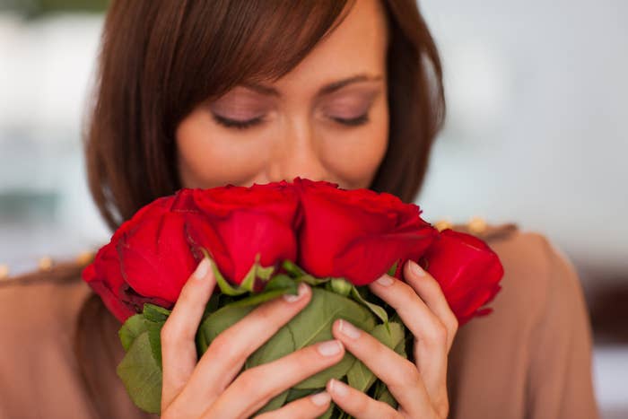 Woman smelling a bouquet of red roses, eyes closed, expressing enjoyment