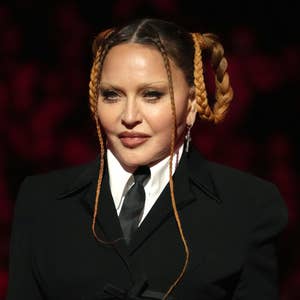 Person in a tailored suit with braided hair, black tie, and hoop earrings