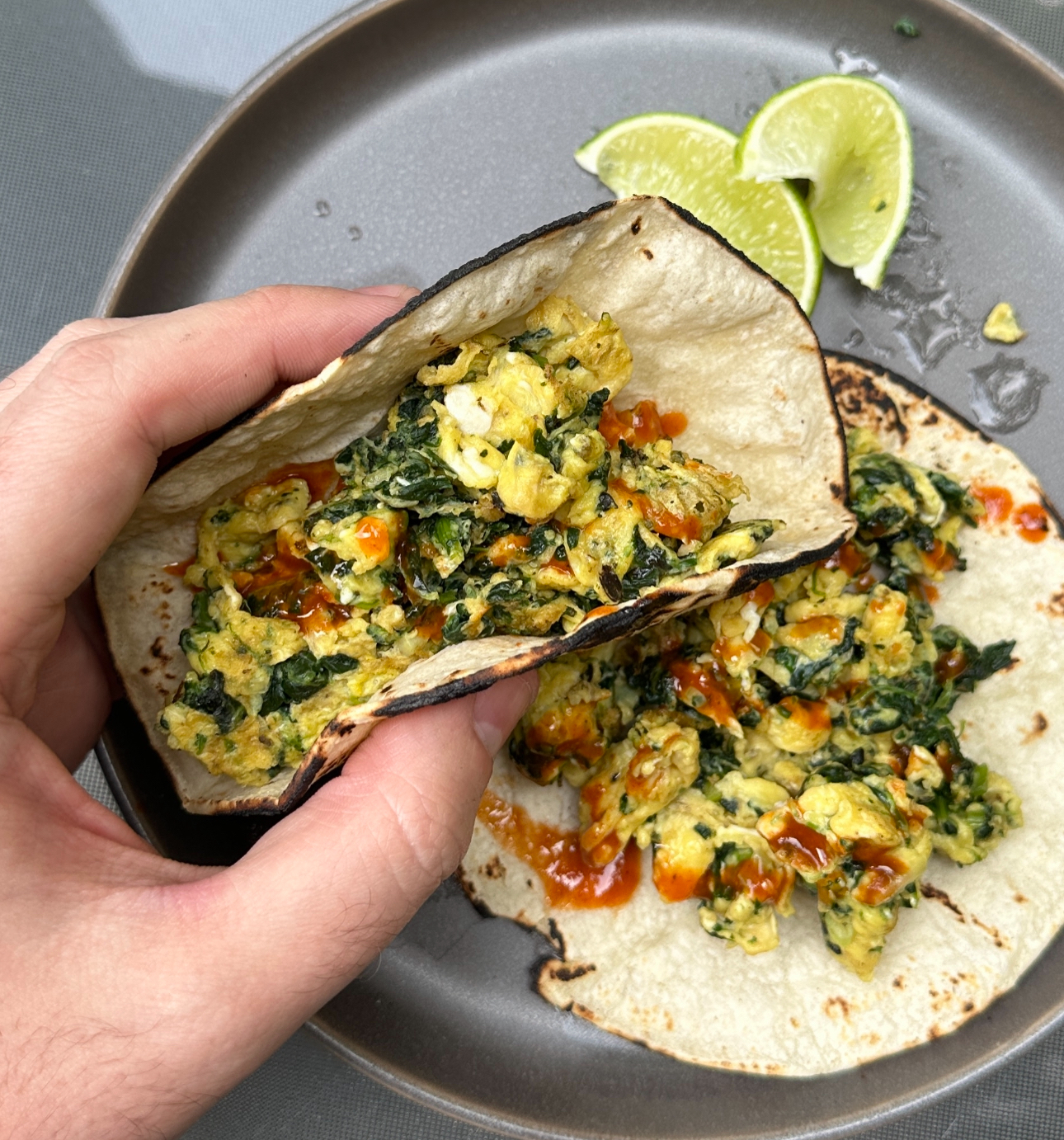 Hand holding a taco filled with scrambled eggs and spinach, with a lime wedge on the side