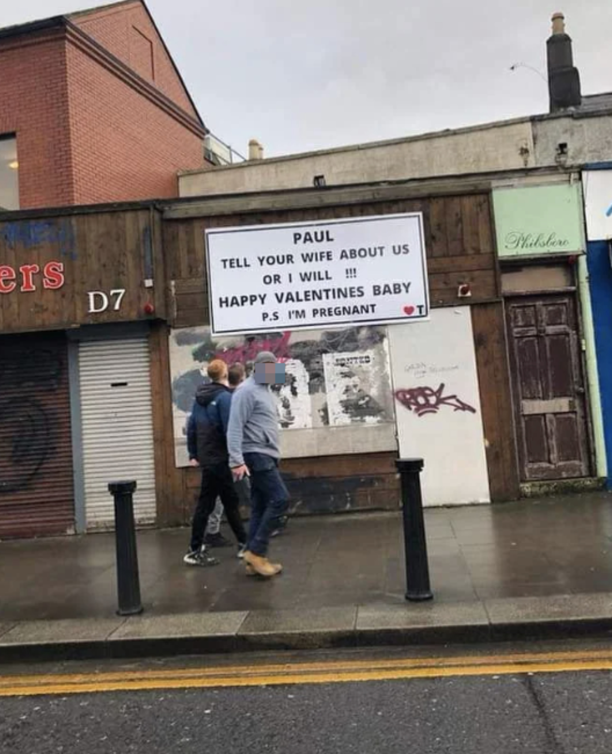 Billboard with a message to Paul about telling his wife of a pregnancy revelation, with two people walking by