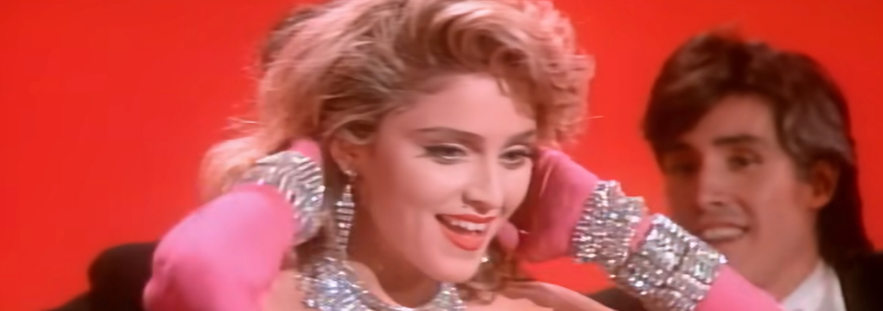 Madonna in a dress and long gloves and a diamond necklace, smiling in  the Material Girl music video