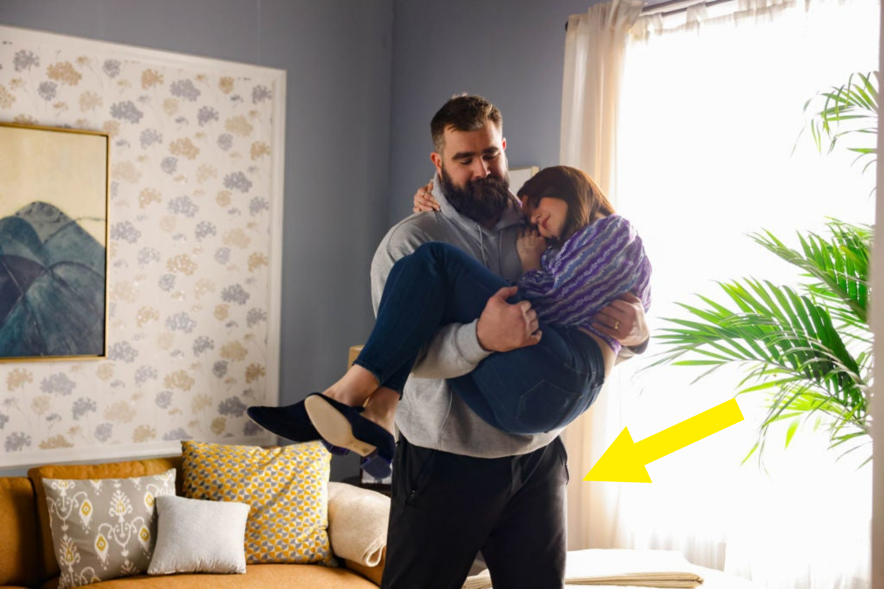 Jason Kelce holding a woman in a comforting embrace in a cozy room during an SNL sketch