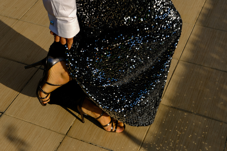 Person in a glittering sequined skirt with black heels standing on a paved surface