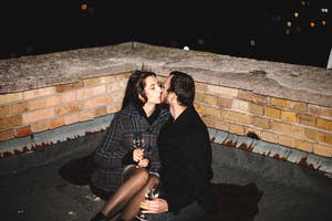 Two people sitting close and kissing on a rooftop at night