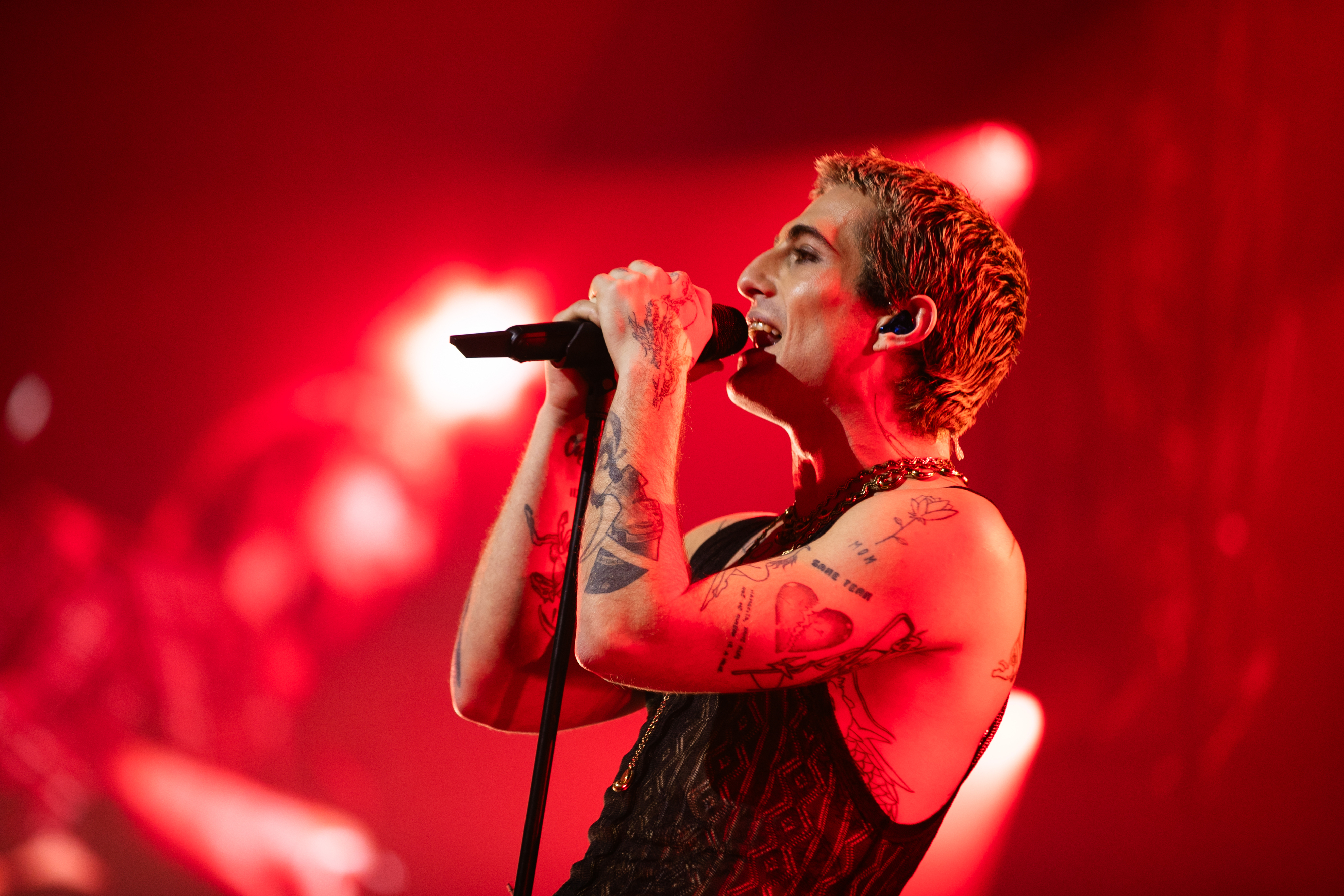 Damiano David en el escenario con micrófono, tatuajes visibles y top de encaje