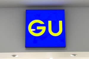 Sign with "GU" logo on blue background mounted on a wall with lights below it