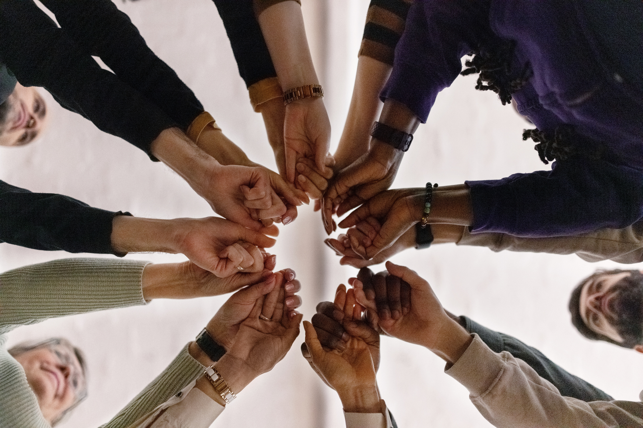 Group of people standing in a circle with their hands together in the middle, suggesting teamwork or unity