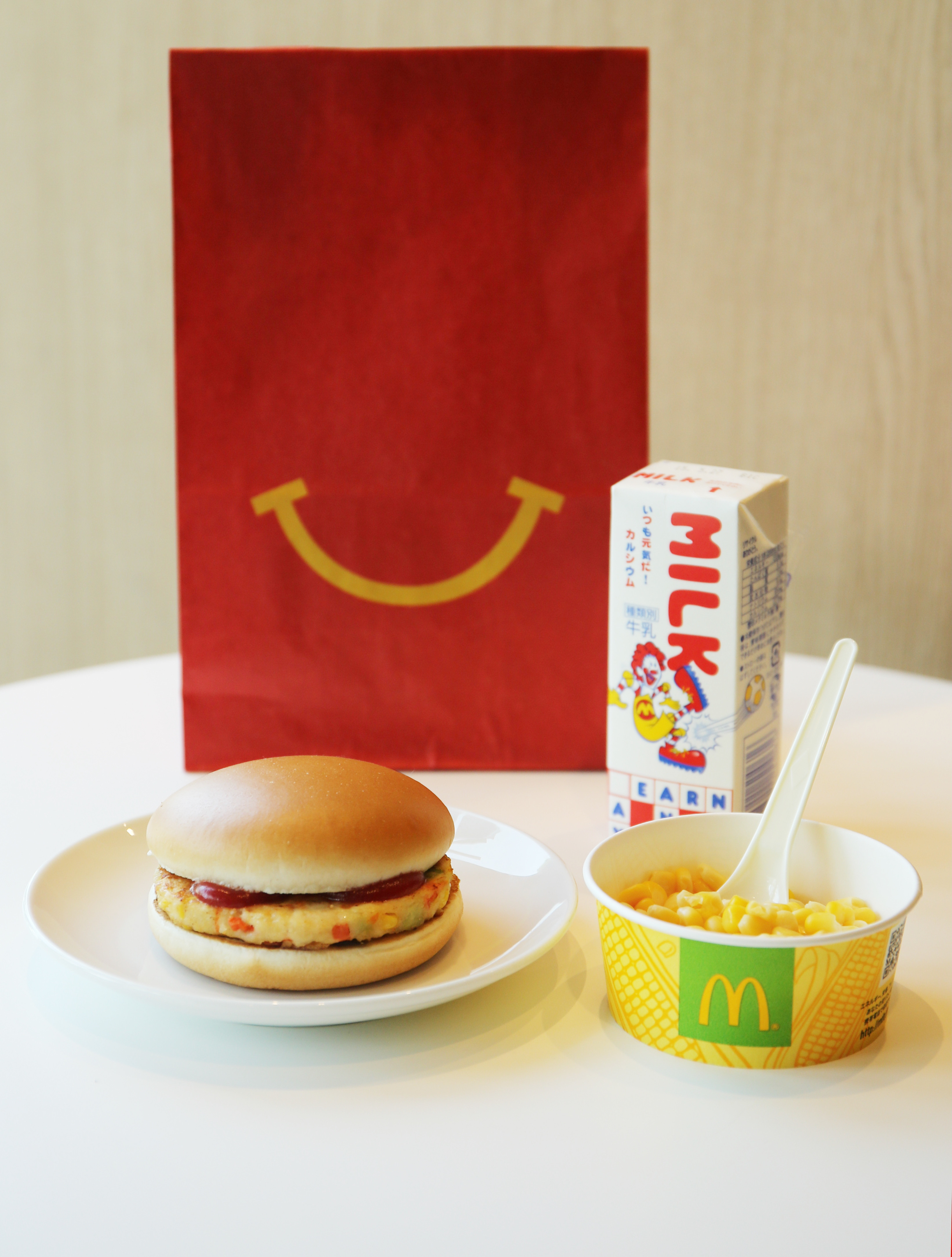 マクドナルドの食事がテーブルに置かれています。ハンバーガー、コーン、牛乳パックが含まれます。