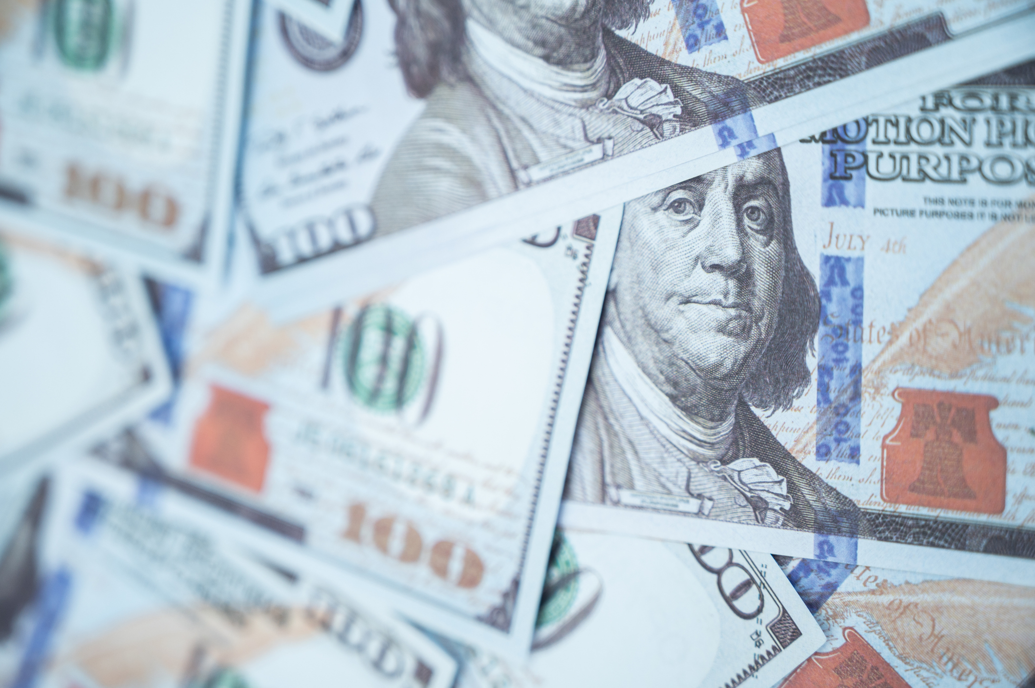 Multiple US $100 bills spread out with focus on the portrait of Benjamin Franklin