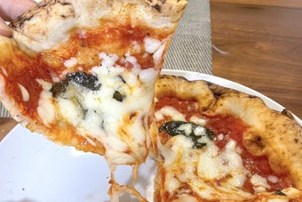 ピザの一切れが手で持ち上げられており、チーズが伸びている様子です。