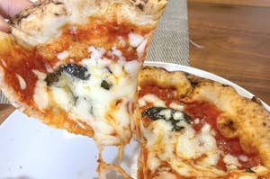 ピザの一切れが手で持ち上げられており、チーズが伸びている様子です。